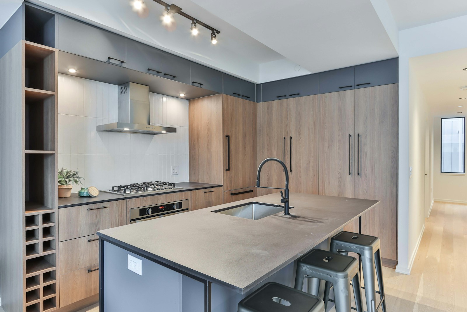 Modern kitchen with a large island featuring a black countertop and a built-in sink. The kitchen includes wooden cabinets, a stainless steel stove with a hood, a built-in oven, and multiple storage compartments. Bar stools are placed by the island. Expert building services ensure everything is perfectly installed.